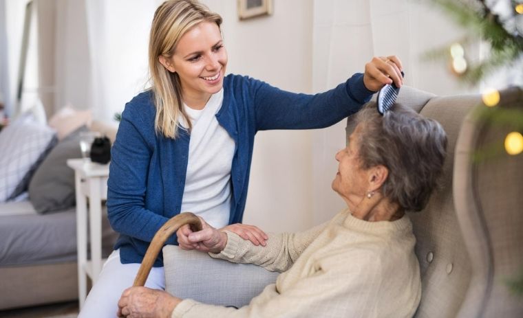 A smiling caregiver brushes an elderly woman’s hair, showing compassionate family caregiver support in Pennsylvania