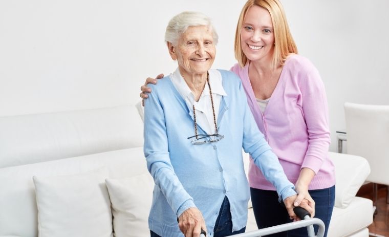 A smiling family caregiver standing beside an elderly woman using a walker, representing compassionate family caregivers helping seniors live safely at home