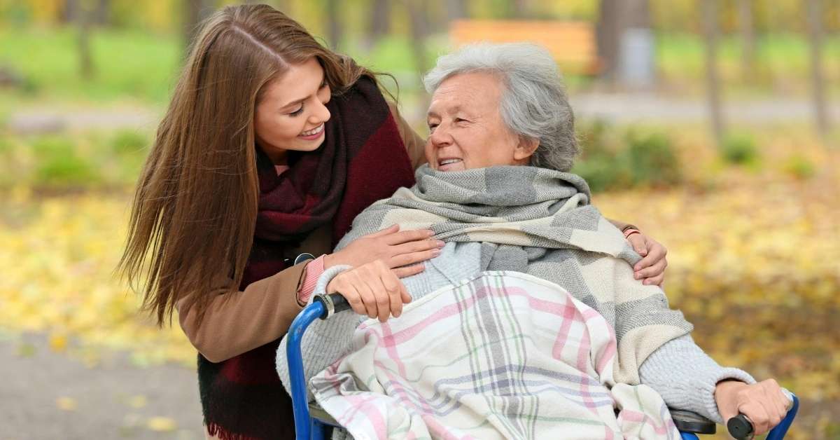 A young woman smiling and caring for her elderly mother in a wheelchair during autumn, representing balancing work and caregiving for Pennsylvania families.