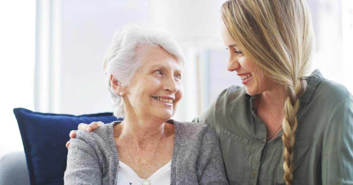 Smiling elderly woman sitting with a supportive young caregiver at home, representing the rights and responsibilities of home care patients in Pennsylvania.
