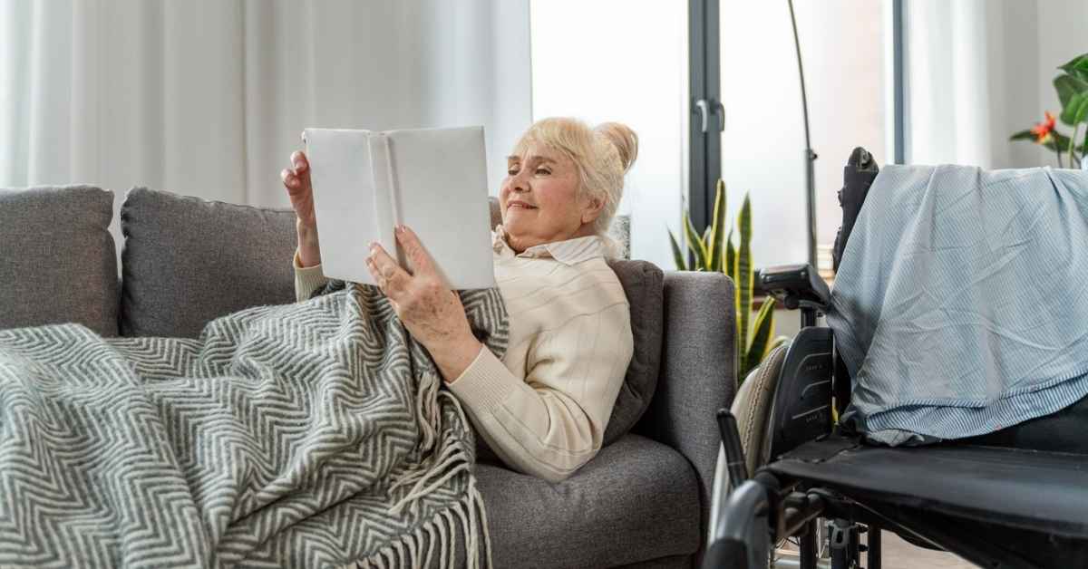 Senior woman staying warm at home while reading on a couch, demonstrating winter safety tips for seniors to remain comfortable and protected indoors.