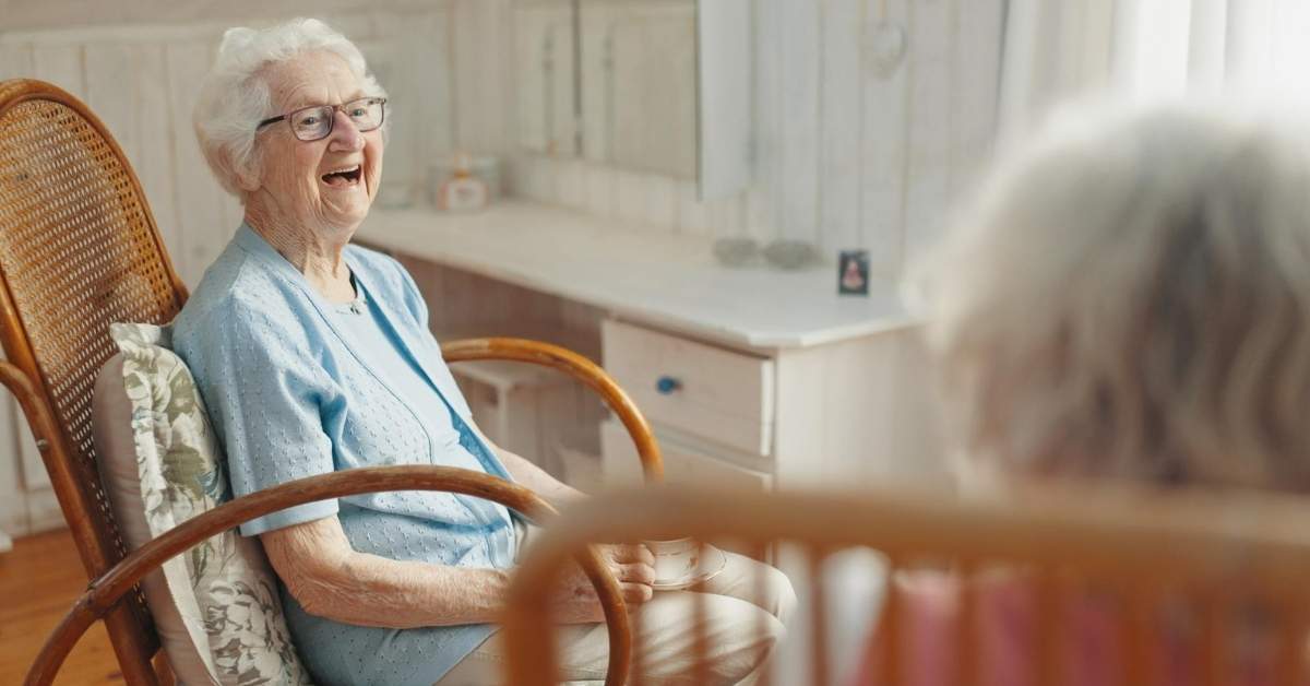 Elderly woman smiling while sitting at home with a caregiver, showing a moment that reflects when an aging parent needs home care support.