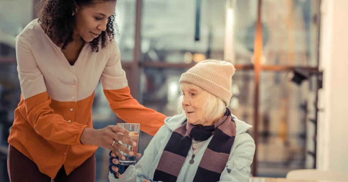 Home caregiver assisting senior woman with drinking water to support daily independence and safety at home.